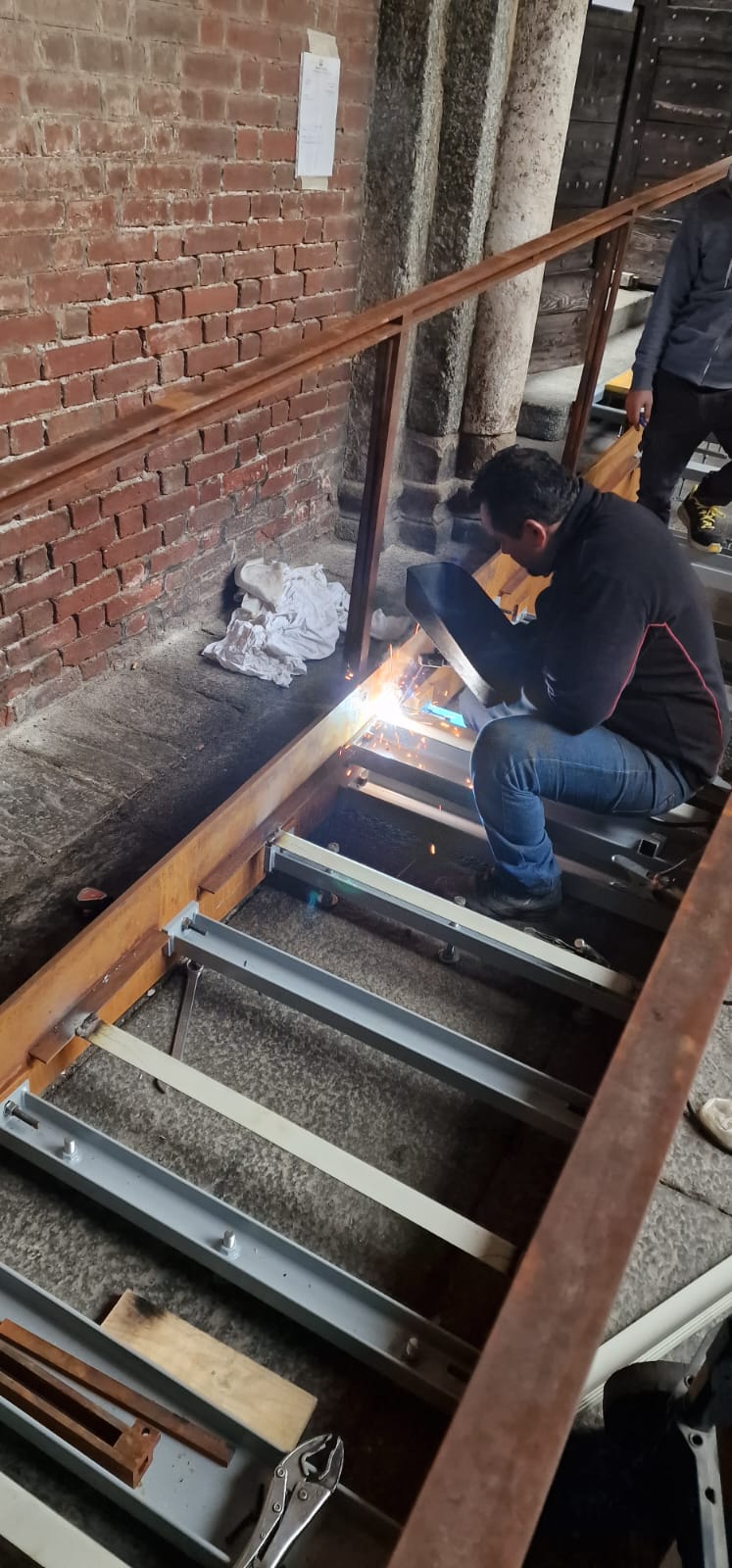 Saldatura del telaio di una rampa metallica accanto a un muro in mattoni rossi realizzata da Gamma Metallica