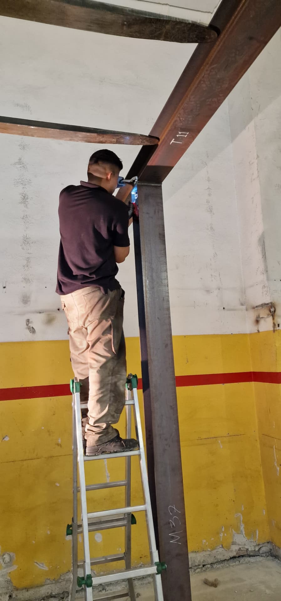 Operatore su scala in alluminio al lavoro sul giunto tra travi in acciaio durante il montaggio di una struttura metallica realizzata da Gamma Metallica